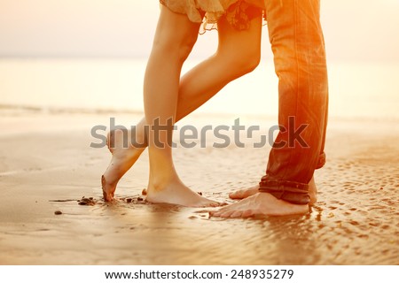 A young  loving  couple hugging and kissing on the beach at sunset. Two lovers, man and woman barefoot near the water. Summer in love