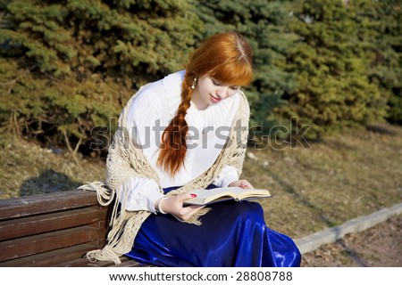 The image of a girl who reads the book in the park on a bench in a sunny day