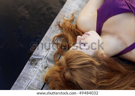Images of a beautiful red-haired girl on the pier in a purple dress