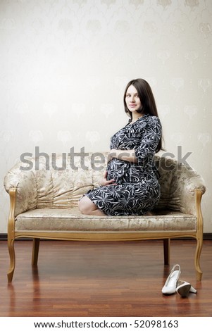 The image of a beautiful pregnant woman sitting on a vintage couch