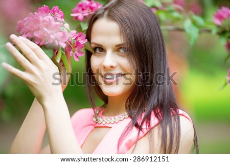 Young spring fashion woman. Trendy girl in the flowering trees in the spring summer garden. Springtime or summertime. Lady in spring landscape background. Allergic to pollen of flowers Spring allergy