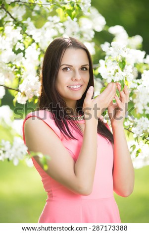 Young spring fashion woman. Trendy girl in the flowering trees in the spring summer garden. Springtime or summertime. Lady in spring landscape background. Allergic to pollen of flowers.Spring allergy