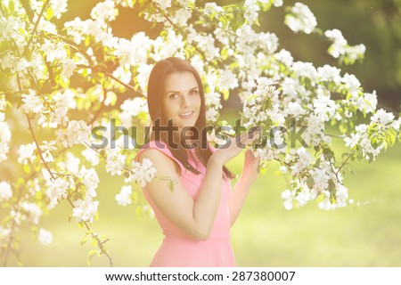 Young spring fashion woman. Trendy girl in the flowering trees in the spring summer garden. Springtime or summertime. Lady in spring landscape background. Allergic to pollen of flowers. Spring allergy