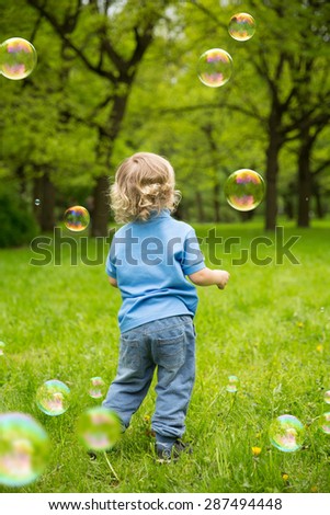 Cute curly baby with soap bubbles children playing running Child playing outdoors in the flowering trees in spring summer garden.  Springtime or summertime. Boy in spring summer landscape background.