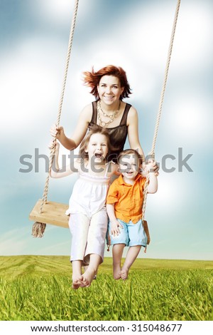 Family fun. Mom, daughter, son laughing on a swing against the sky and clouds. Family weekend vacation.