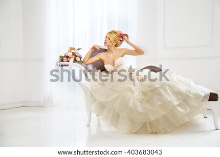 Beautiful fashion model. Sensual bride. Woman with wedding dress, hair and make up. Waiting for groom on background of window. Natural manicure. Beauty spring girl with bouquet of flowers in hands