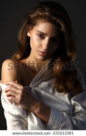 Fashion model posing on a dark background in a white silk blouse  in sexy atmosphere light