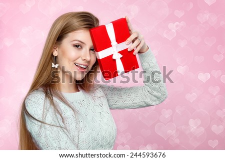 Sweet blonde woman holding a red gift box. Valentines Day.  heart shaped bokeh background Joyful