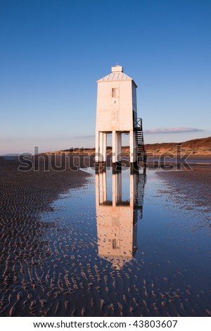 Wooden lighthouse built out of oak on the sandy beach at Burnham-on-Sea at sunset. Th structure is reflected in a tidal pool.