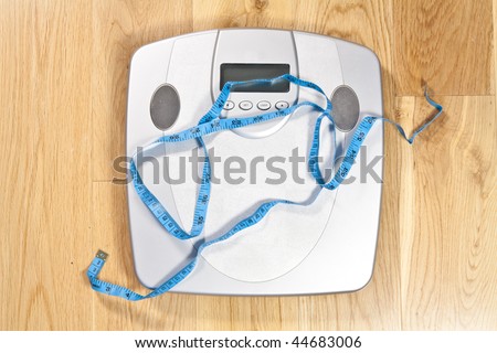 Modern electronic scales with blue tape measure across it on a wooden floor symbolising dieting
