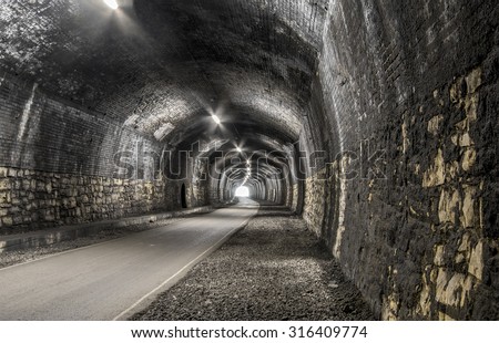 HDR old brick built railway tunnel with soot covered walls and with the exit glowing in the distance