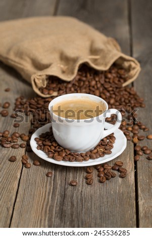 Coffee bag full of coffee beans and white cup of coffee in front. Placed on an old wooden background.