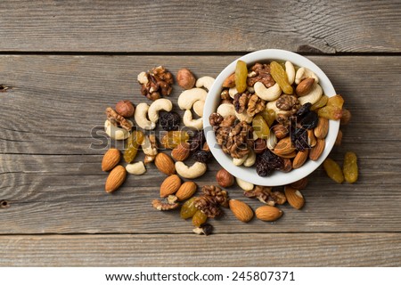 Nuts and dried fruits in a white bowl on a wooden table. View from above.