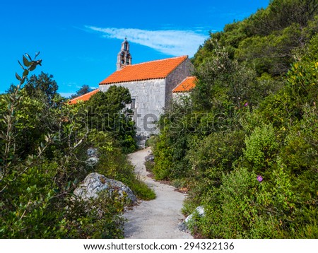 Landscape photo of a small path leading to a small church with lots of vegetation around and blue sky above.