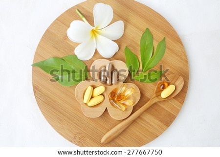 Herbal supplements and vitamins  on wooden tray, decorated with white flowers and green leafs background as white cotton cloth