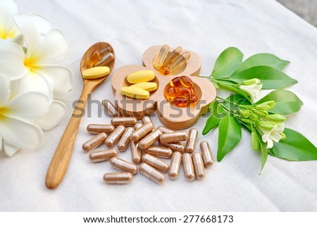 Herbal supplements and vitamins  on wooden tray and wooden spoon, decorated with white flowers and green leafs background as white cotton cloth