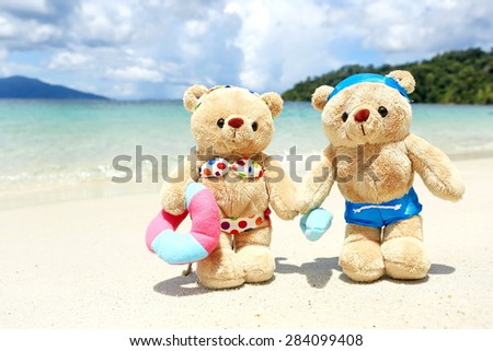 teddy bears in swimsuit and bikini walking on sand beach , background mountain and blue sky by the sea