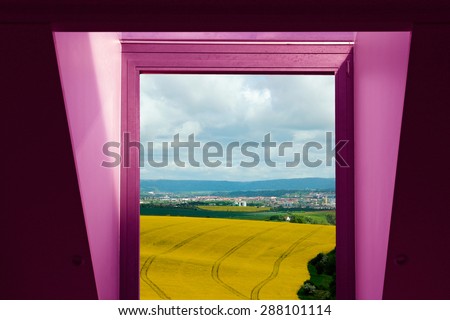 Window with a view of amazing alfalfa meadows. Purple / violet window casement  vigorously contrasts to yellow fields. Optimistic lifestyle, environmental or ecological motif