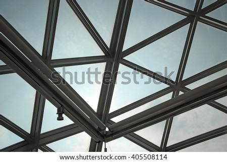 Unrecognizable fragment of modular / structural glass ceiling against sky. Glazed aluminum structure with triangular pattern. Abstract architectural background composition.