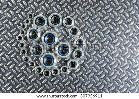 Spiral arrangement of various sizes of Nylon locking steel nuts on a patterned steel background.