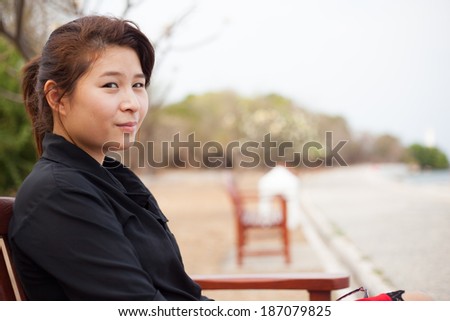 Asian women black shirt. Sitting on wooden bench. Adjacent to the corridor of the park.