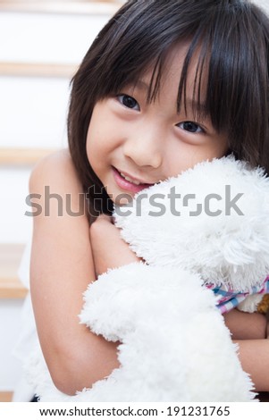 Girl are hugging the doll. Sitting in the stairs and hugging teddy bear white.
