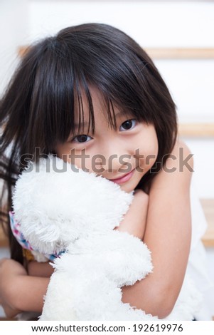 Girl are hugging the doll. Sitting in the stairs and hugging teddy bear white.