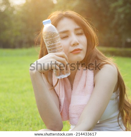 Woman Sitting and holding a bottle of water. Sitting on grass in the park after jogging. In the evening