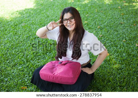Female student sitting on the lawn. Pink bag was placed on it.