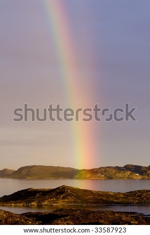 The end of a rainbow and it\'s reflection in the water. There are actually a second weaker rainbow comeing up on the right and in a slightly larger arc. Very beautiful i real life.