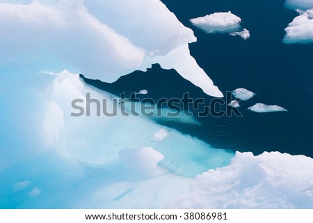 A white iceberg drips in to to the deep blue water. You can see the iceberg below the water surface in beautiful turquoise colors.
