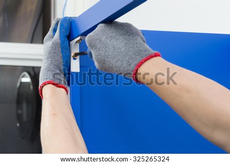 Worker assembling a metal shelf, screwing screw using a manual screwdriver.Do-it-yourself (DIY) concept.