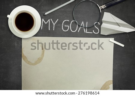 My goals concept on black full frame blank blackboard with coffee cup. empty paper and magnifying glass