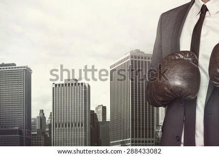 Businessman in boxing gloves and suit on cityscape background