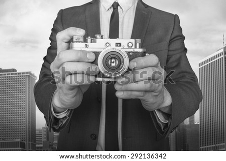 Businessman taking a photo with vintage camera on cityscape background black and white photo