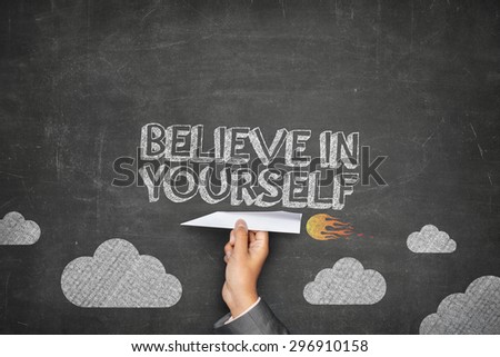 Believe in yourself concept on black blackboard with businessman hand holding paper plane
