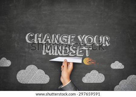 Change your mindset concept on black blackboard with businessman hand holding paper plane