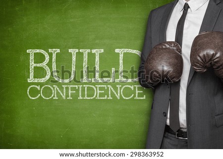 Build confidence on blackboard with businessman wearing boxing gloves