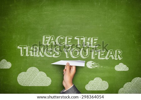 Face the things you fear concept on green blackboard with businessman hand holding paper plane
