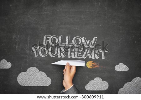 Follow your heart concept on black blackboard with businessman hand holding paper plane
