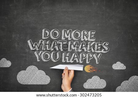 Do more of what makes you happy concept on black blackboard with businessman hand holding paper plane