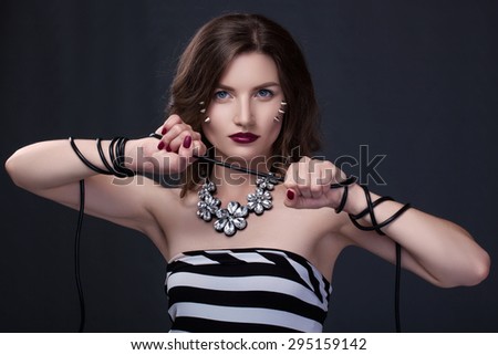 Girl with spikes on her face, bound with wire in a striped black and white dress