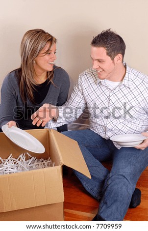 Young Couple Sat On The Floor Unpacking Boxes In Their New Home