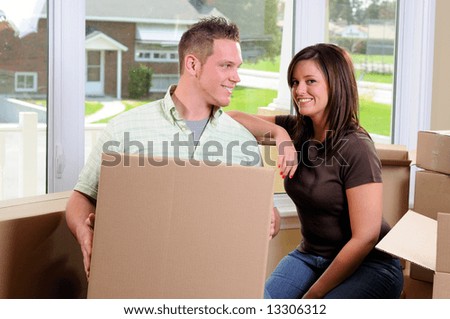 Young Couple Moving Into Their New Home Surrounded By Cardboard Boxes