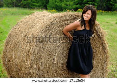 Beautiful Woman Wearing A Black Cocktail Dress Leaning Against A Hay Bale