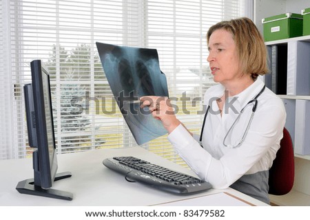 A Middle Age Female Doctor Working With A Computer In Her Office Holding A Chest X-Ray