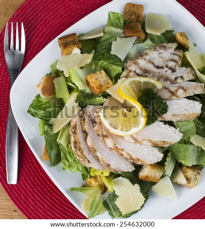 A delicious gluten free chicken Caesar salad on a white plate and red place mat.  Fork is placed off to the side.