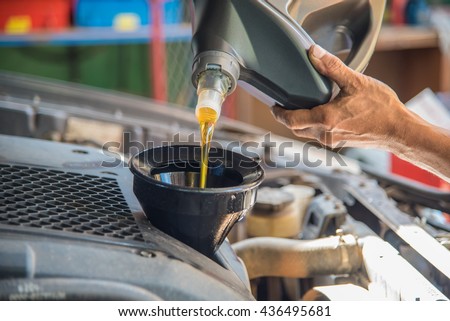 Car maintenance servicing mechanic pouring new oil lubricant into the car engine, A mechanic pours fresh oil into a car engine as part of its maintenance.