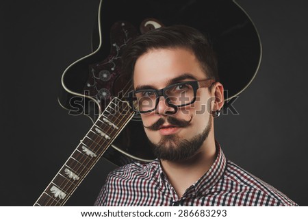 handsome guy with beard and mustache with acoustic guitar on dark background in studio