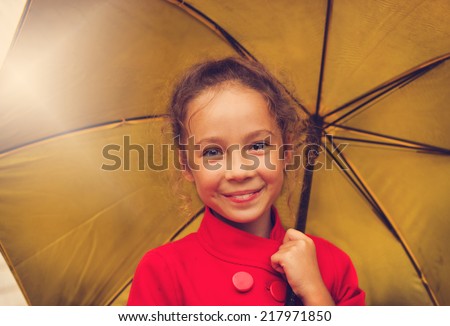 vintage portrait of happy school girl in a red jacket holding an yellow umbrella in autumn day